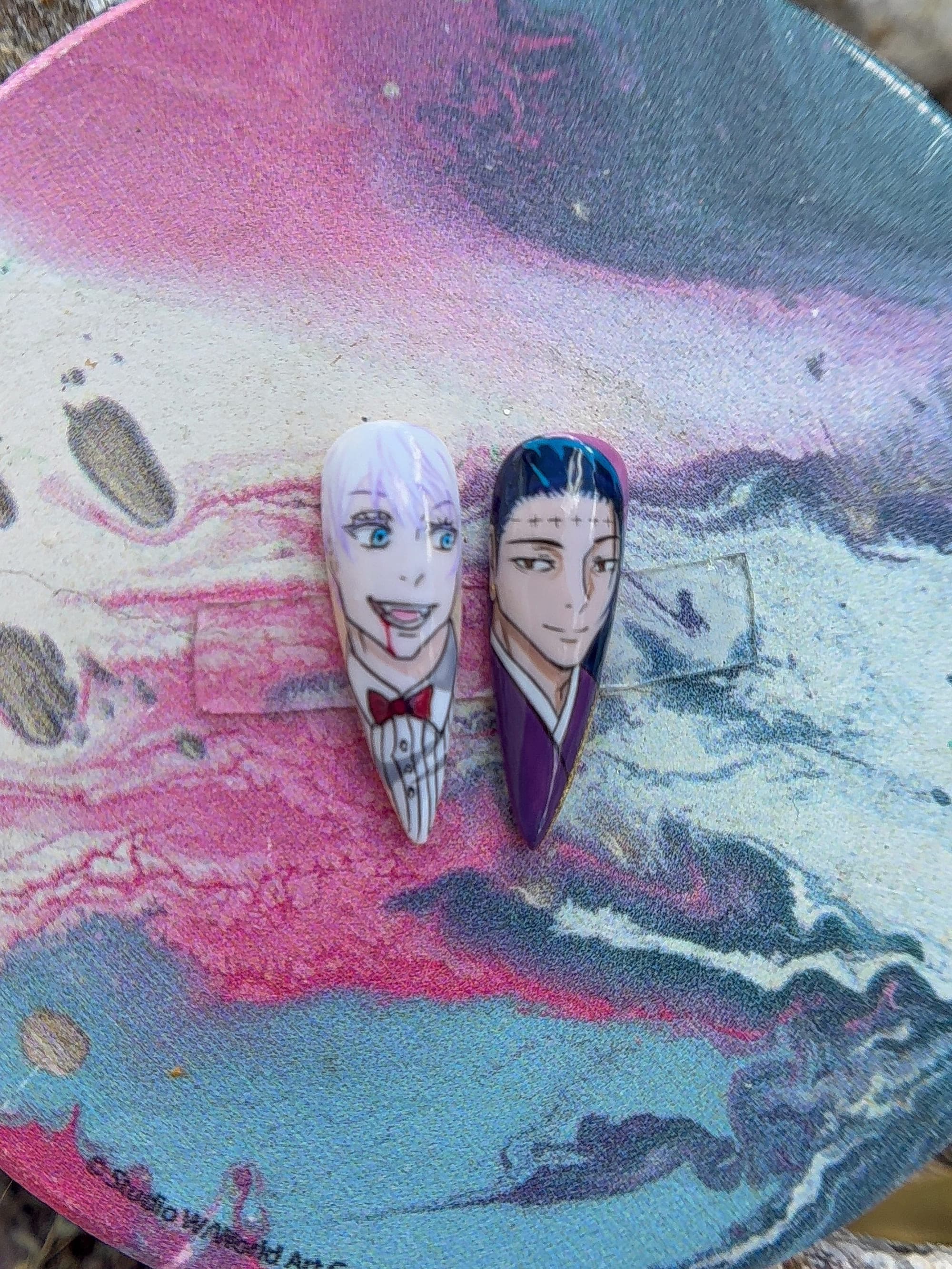Hand-painted Gojo and Geto portrait nails resting on a marbled tray