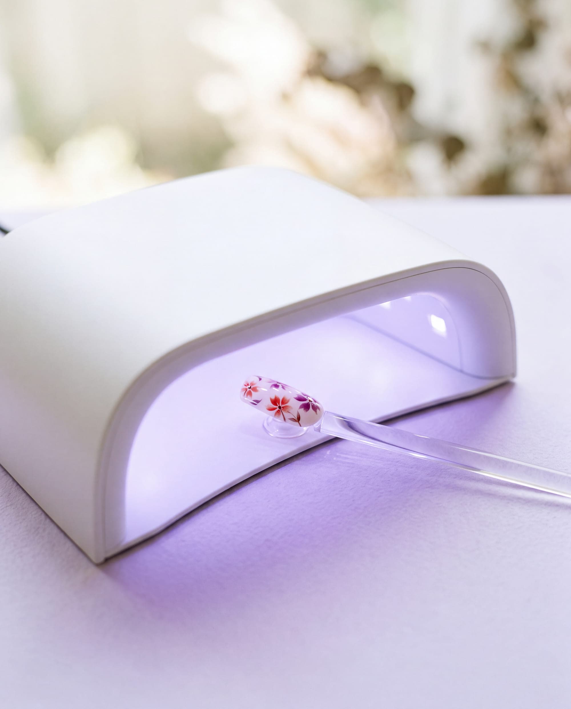 A hand-painted nail tip curing under a softly glowing LED lamp